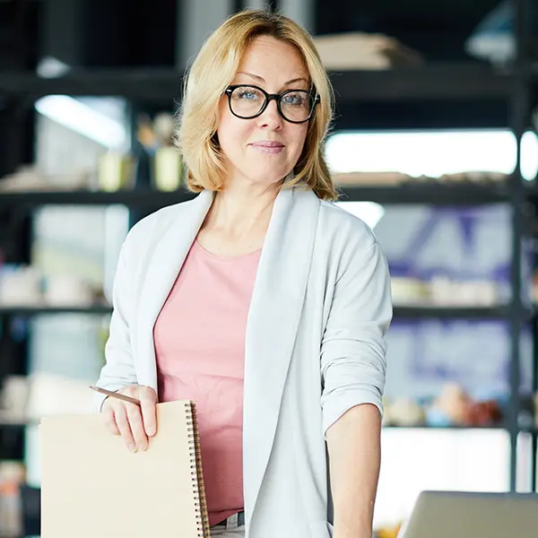 Confident woman with glasses holding a sketchpad in a creative studio